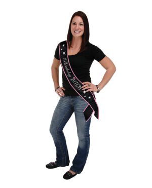 Woman standing and smiling wearing a black T-shirt, jeans, and a birthday sash.