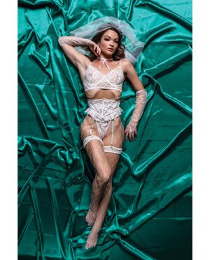 A woman posing in sophisticated white lingerie, complemented with long gloves, lying on a luxurious emerald green satin sheet.