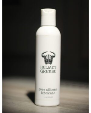 A white bottle of 'Helmet Grease' pure silicone lubricant on a dark background