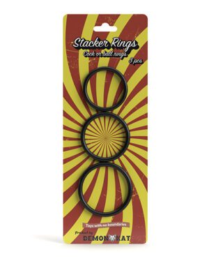Packaging for "Stacker Rings" featuring three black rings against a red and yellow burst background with the text "Stacker Rings – Cock or ball rings, 3 pcs" and "Toys with no boundaries" by DEMONIQ.