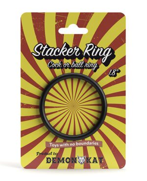 A product packaging for a "Stacker Ring" with a black ring centered on a red and yellow radial burst background. Text indicates it's a "Cock or ball ring" measuring .8" and is by "DEMONQKA" with the tagline "Toys with no boundaries." A small logo featuring a stylized cat's face appears at the bottom with the brand name.
