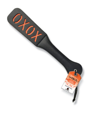 A black silicone spatula with the letters "OXOX" written in red, with a white and orange product tag attached that reads "CRUCIAL DETAIL THE ORBITAL TRILOGY XOXO."