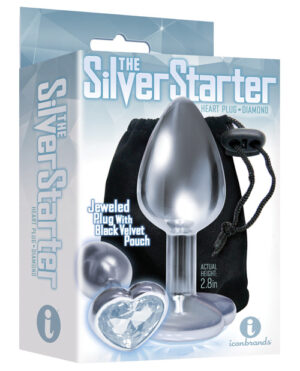 Product packaging for "The Silver Starter Heart Plug + Diamond," featuring a silver-colored jeweled plug with a heart-shaped base, accompanied by a black velvet pouch, with the actual height of the item indicated as 2.8 inches.