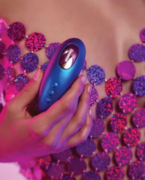 A person's hand holding a sleek blue beauty device against a backdrop of sparkling purple sequins.