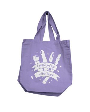 A purple tote bag with a graphic of cooking tools and the phrase "I still play with toys".