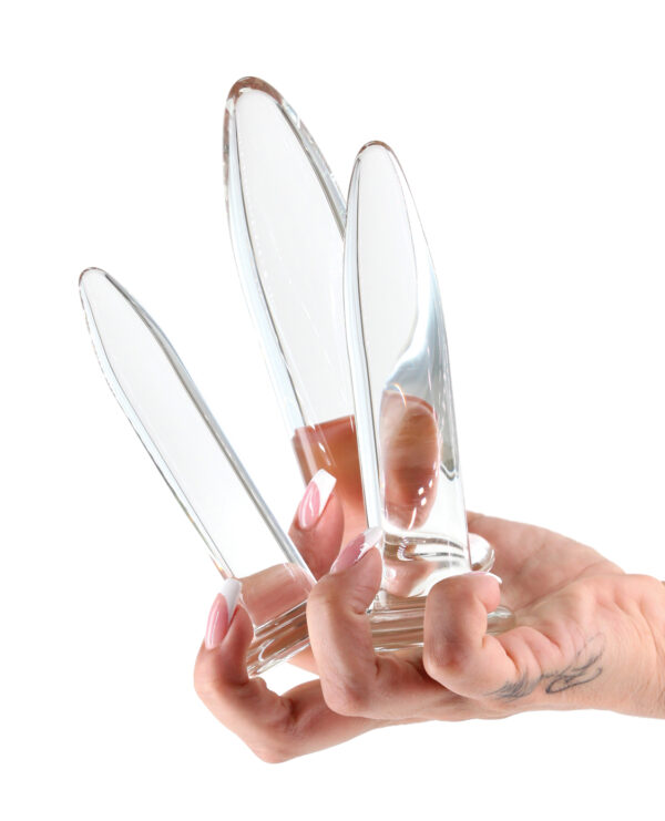 A hand holding three transparent glass pleasure objects, showcasing their sleek design against a white background.