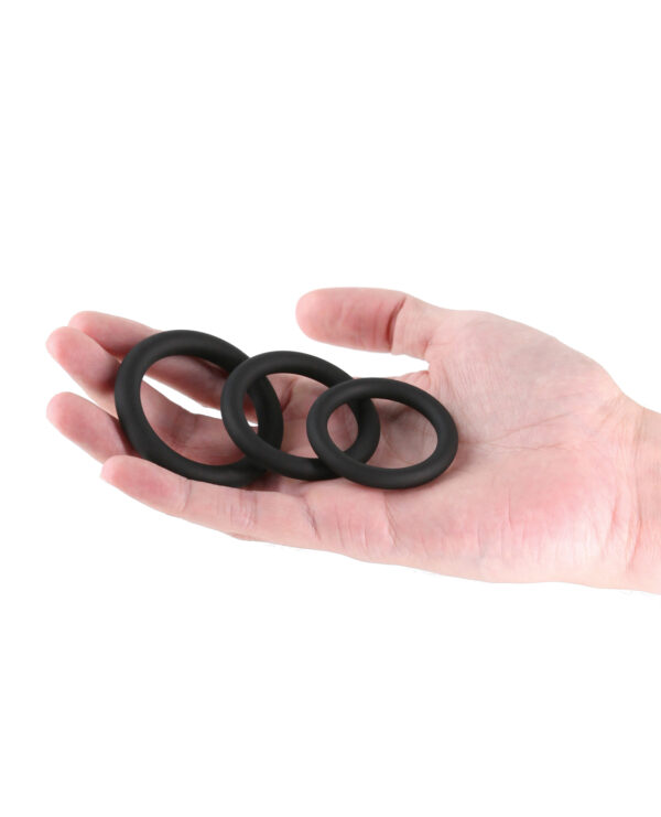 A hand holding three black silicone rings of varying sizes against a white background.