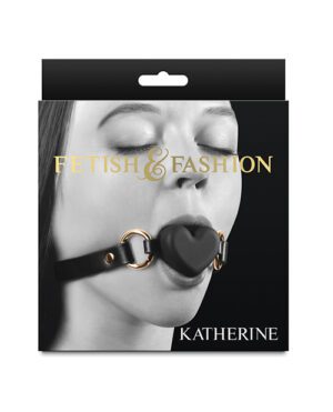 Product packaging featuring a close-up image of a woman's lower face with a black gag with a heart-shaped middle in her mouth, with the words "FETISH & FASHION" above and the name "KATHERINE" below. The packaging has a black top with a hang hole.