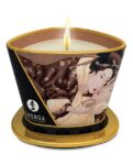 A lit candle with an illustration of a couple embracing on the exterior, placed on a gold stand with the label "SHUNGA EROTIC ART" at the base.