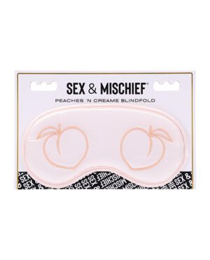 A light pink blindfold with peach designs over the eye areas, labeled 'SEX & MISCHIEF PEACHES 'N CREAME BLINDFOLD' in a product packaging.
