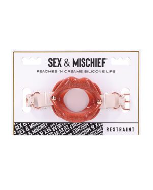 Packaging for a "Sex & Mischief" branded product featuring silicone lips with straps, labeled as "Peaches 'n Creme Silicone Lips" with the word "restraint" visible at the bottom.