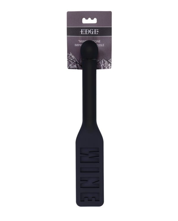 A black silicone spatula with the word "WINE" cut out from the flat end, attached to a hanging retail card that reads "EDGE" on an isolated white background.