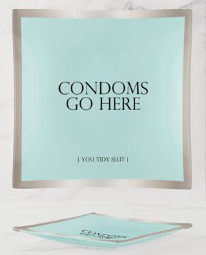 A mint green square dish with the phrase "CONDOMS GO HERE" and the caption "[ YOU TIDY SLUT ]" printed in black, resting on a marble surface.