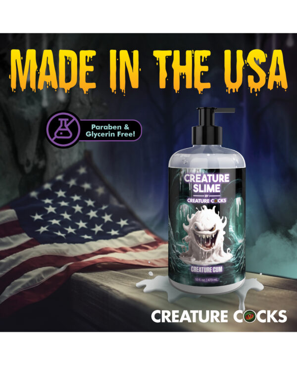 A bottle of Creature Slime by Creature Cocks, with a spooky design, placed on a wooden surface in front of an American flag.