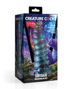 This image shows an adult novelty product called "Creature Cocks Chrysalis Silicone Dildo" in its packaging. The packaging features a vibrant and colorful fantasy-themed backdrop with an image of the caterpillar-shaped dildo prominently displayed through a clear section. Text on the packaging includes product name and taglines.