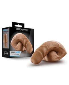 This image features the packaging and product of a "PERFORMANCE 5 INCH PACKER" by Blush. The product is a realistic prosthetic, displayed both in and out of the black box packaging, which emphasizes comfort and has a beige skin tone.